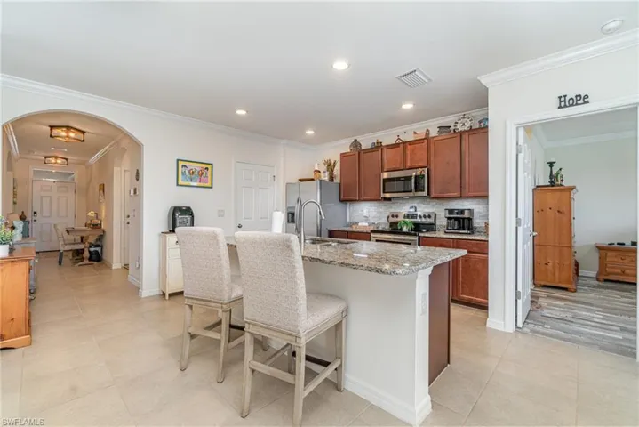 Kitchen with crown molding, light stone countertops, stainless steel appliances, and a center island with sink