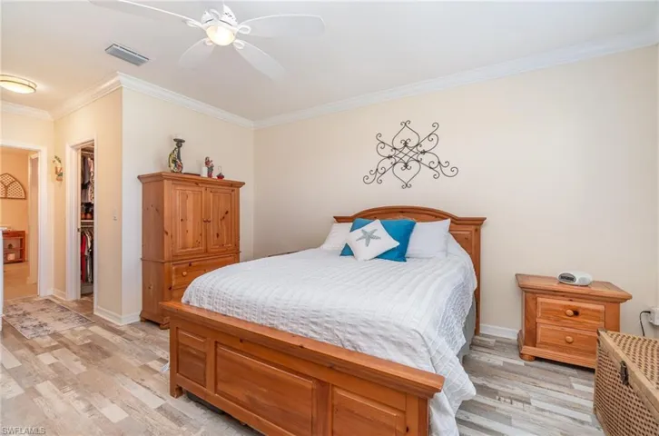 Bedroom featuring light hardwood / wood-style floors, crown molding, a spacious closet, and ceiling fan