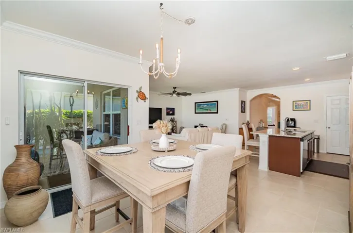 Dining room with light tile patterned flooring, ornamental molding, sink, and ceiling fan with notable chandelier