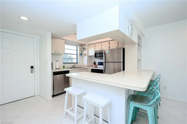 Kitchen featuring light tile patterned floors, appliances with stainless steel finishes, a breakfast bar area, and kitchen peninsula