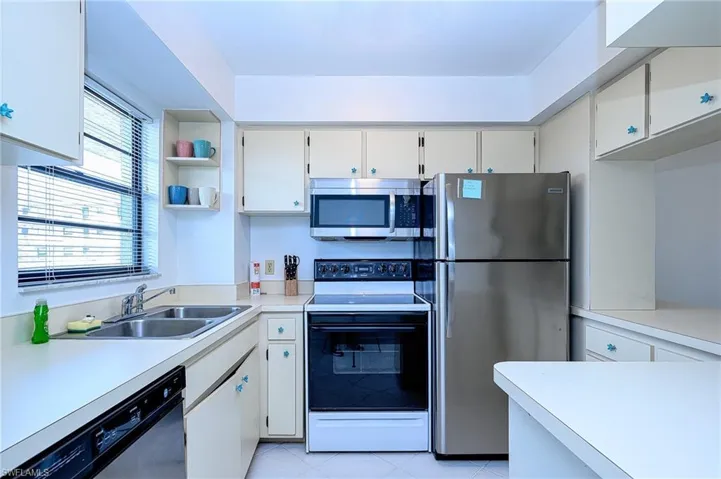 Kitchen featuring sink, stainless steel appliances, light tile patterned flooring, and white cabinetry
