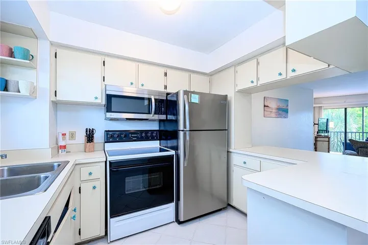 Kitchen with sink, stainless steel appliances, light tile patterned flooring, and white cabinetry