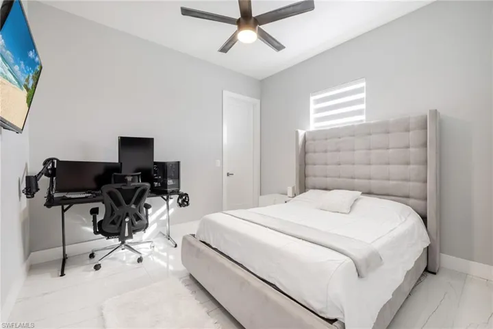 Bedroom featuring an office area, a ceiling fan, and light marble finish flooring