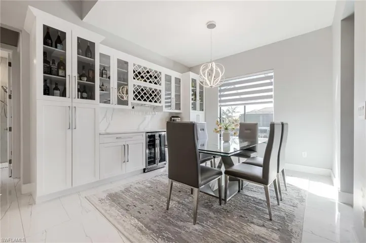 Dining area featuring beverage cooler, hanging lights, light marble finish flooring, and a dry bar