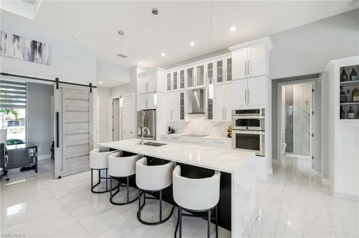 Kitchen with a barn door, glass fronted cabinets, white cabinets, stainless steel appliances, and light stone counters