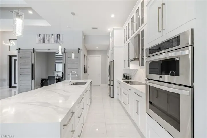 Kitchen with stainless steel appliances, glass fronted cabinets, white cabinetry, a large island, and a barn door