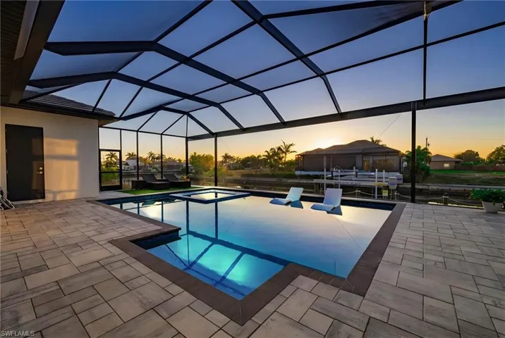 Pool at dusk with a sunroom, a lanai, a patio, and a pool with connected hot tub