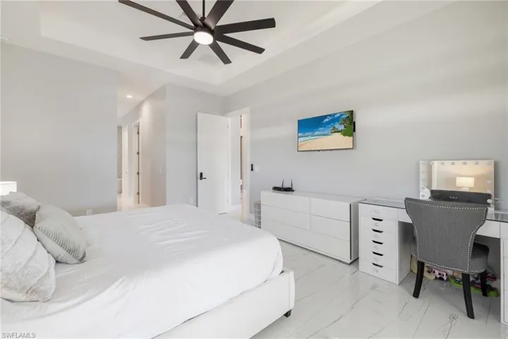 Bedroom with an office area, ceiling fan, light marble finish floors, a raised ceiling, and recessed lighting