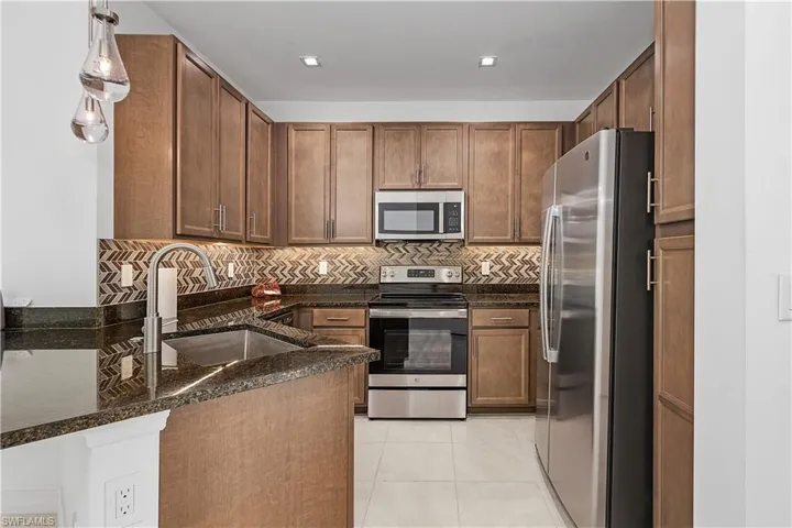 Kitchen with pendant lighting, tasteful backsplash, sink, appliances with stainless steel finishes, and dark stone countertops