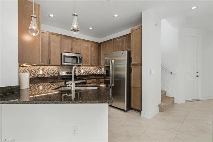 Kitchen featuring light tile patterned floors, kitchen peninsula, decorative light fixtures, appliances with stainless steel finishes, and decorative backsplash