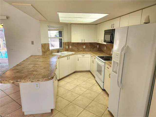 Kitchen with white appliances, a peninsula, tasteful backsplash, light countertops, and light tile patterned floors
