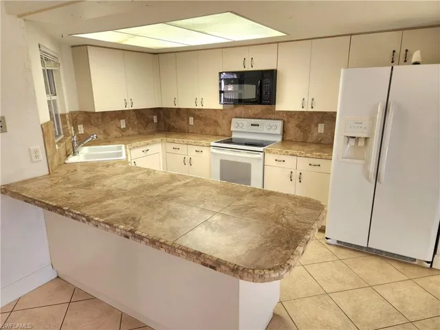 Kitchen featuring white appliances, a peninsula, decorative backsplash, and light tile patterned floors