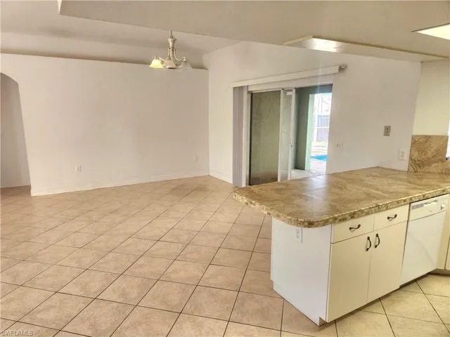 Kitchen with decorative light fixtures, white dishwasher, a peninsula, light tile patterned flooring, and a chandelier