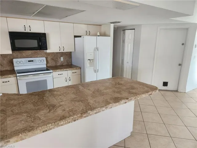 Kitchen with white appliances, light tile patterned flooring, backsplash, tile countertops, and white cabinetry