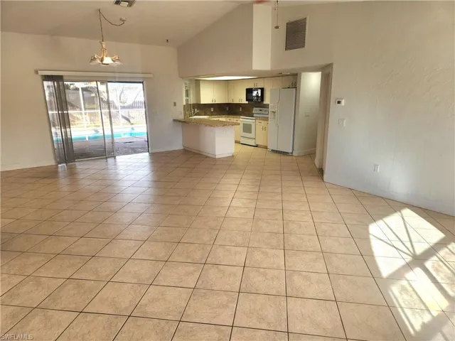 Kitchen featuring open floor plan, white appliances, hanging light fixtures, a peninsula, and a chandelier