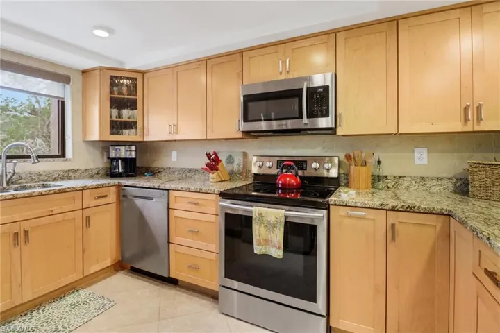 Kitchen with sink, light stone counters, light brown cabinets, and appliances with stainless steel finishes