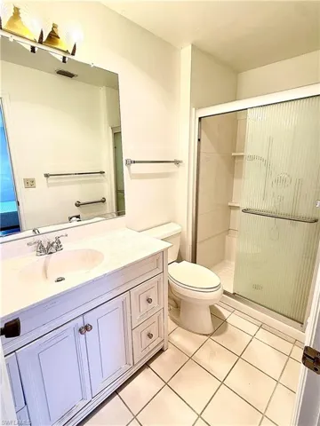 Bathroom featuring a shower with door, vanity, tile patterned floors, and toilet