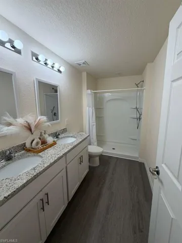 Bathroom featuring a stall shower, dark wood finished floors, double vanity, and a textured ceiling