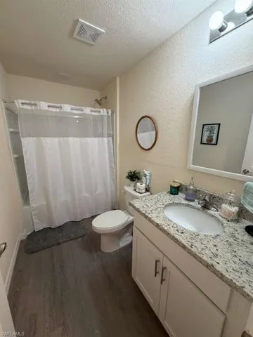 Bathroom with vanity, dark wood finished floors, a textured ceiling, a textured wall, and shower / bath combo with shower curtain