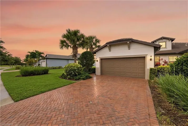 White stucco exterior with a brown garage door, featuring a herringbone brick paver driveway