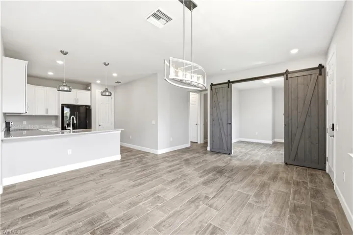 Open-concept living space featuring wood-finish flooring, a kitchen with white cabinetry and dark countertops, recessed lighting, and a contemporary chandelier