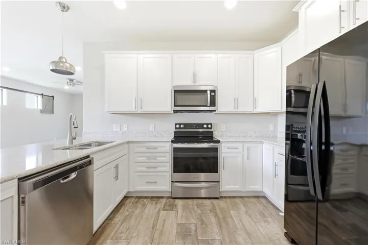 Kitchen featuring white cabinetry, light-toned countertops, stainless steel appliances, and wood-finish flooring