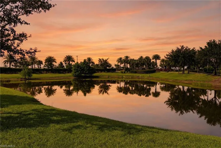 Lush green lawn surrounding a tranquil pond with reflections of various trees and palm trees