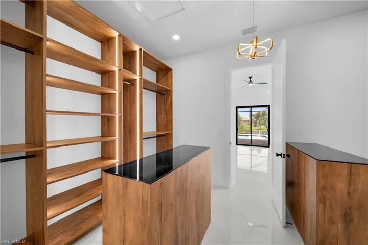 Spacious closet with ceiling fan with notable chandelier and light tile patterned flooring