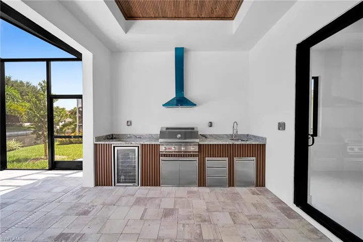 Kitchen featuring sink, wall chimney exhaust hood, built in refrigerator, light tile patterned floors, and a raised ceiling