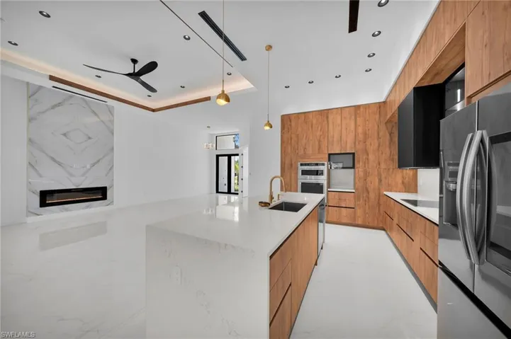 Kitchen featuring stainless steel appliances, decorative light fixtures, sink, an island with sink, and a high end fireplace