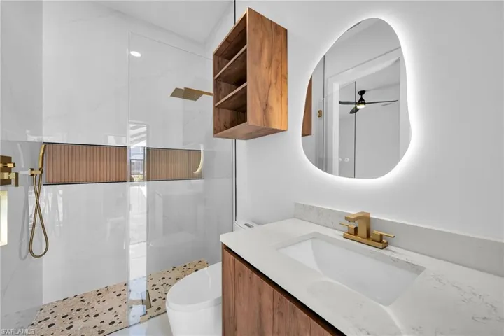 Bathroom featuring ceiling fan, toilet, a shower with shower door, and vanity