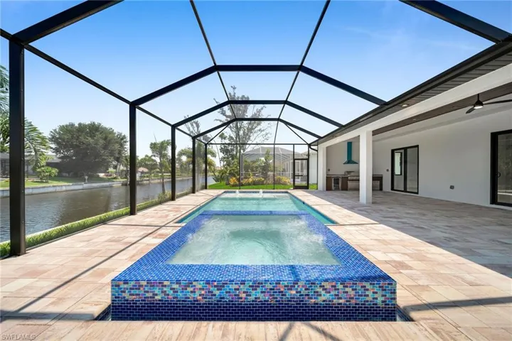 View of pool with glass enclosure, a patio area, a water view, an in ground hot tub, and ceiling fan