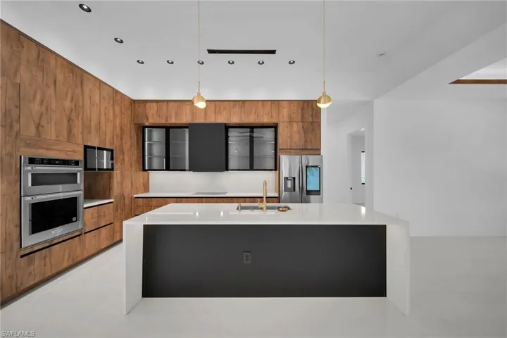 Kitchen featuring light tile patterned flooring, stainless steel appliances, pendant lighting, and a center island with sink