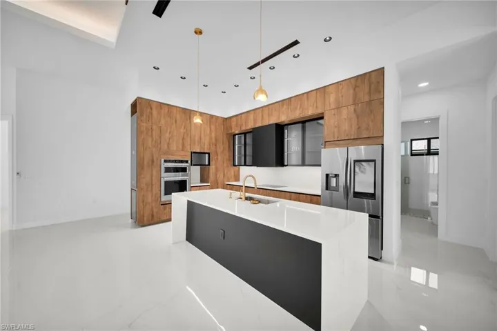 Kitchen with sink, appliances with stainless steel finishes, light tile patterned floors, hanging light fixtures, and a center island with sink