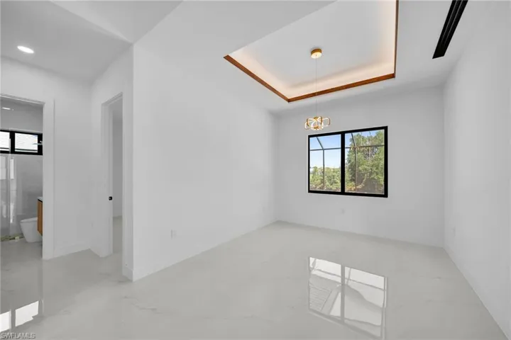 Empty room featuring a tray ceiling, light tile patterned flooring, and an inviting chandelier