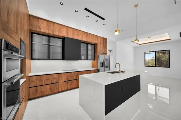 Kitchen featuring sink, appliances with stainless steel finishes, light stone countertops, pendant lighting, and a center island with sink