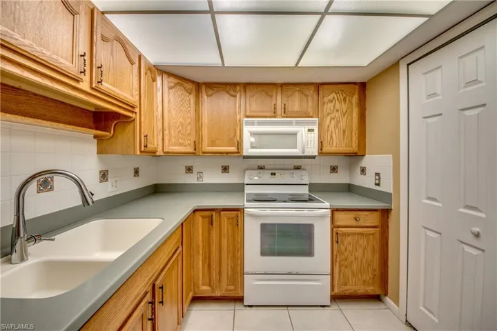 Kitchen with backsplash, white appliances, light tile patterned floors, and sink