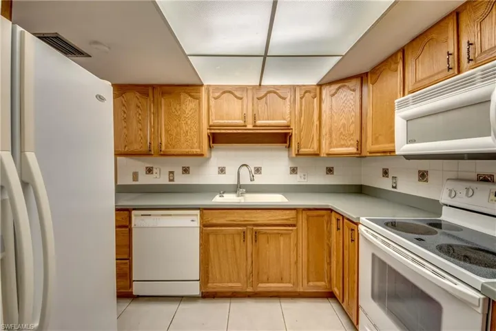 Kitchen featuring white appliances, tasteful backsplash, light tile patterned floors, and sink