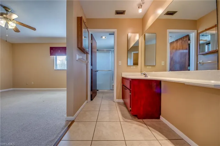 Bathroom featuring ceiling fan, vanity, tile patterned flooring, and an enclosed shower