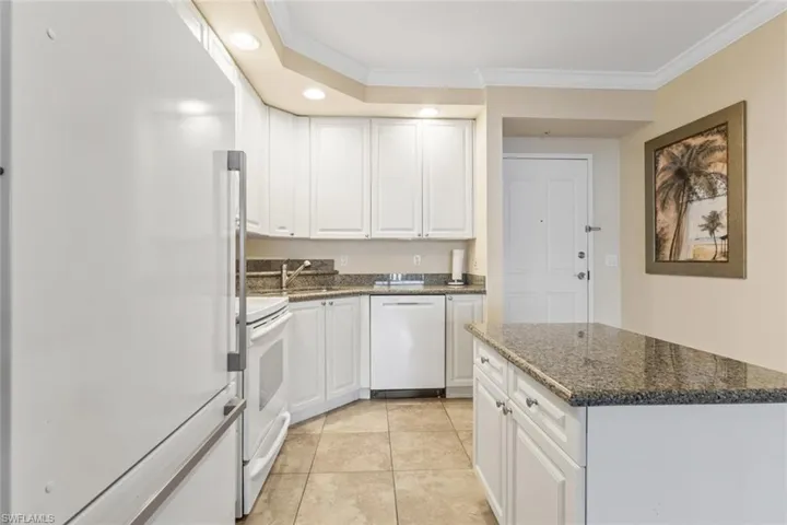 Kitchen with white appliances, crown molding, recessed lighting, dark stone countertops, and white cabinetry