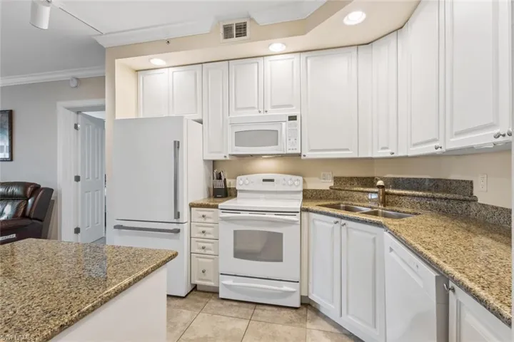 Kitchen with ornamental molding, white appliances, white cabinets, light stone countertops, and light tile patterned floors