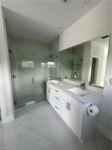 Full bath featuring double vanity, a marble finish shower, and marble finish flooring