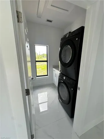 Washroom with cabinet space, light marble finish floors, and stacked washer and clothes dryer