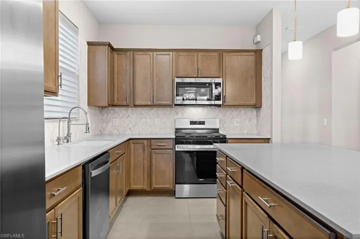 Kitchen with stainless steel appliances, hanging light fixtures, and brown cabinetry