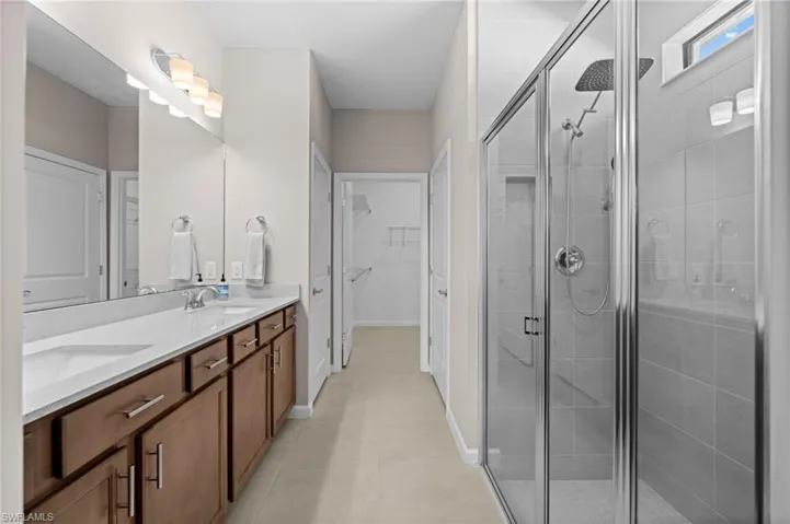 Full bath with double vanity, a spacious closet, a shower stall, and light tile patterned floors