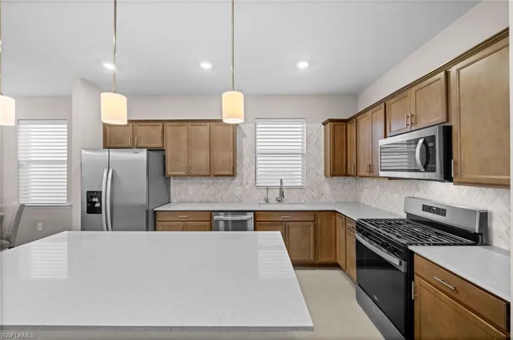 Kitchen featuring stainless steel appliances, decorative light fixtures, decorative backsplash, light stone countertops, and brown cabinets