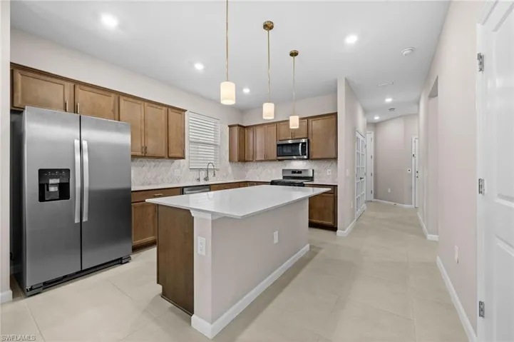 Kitchen with appliances with stainless steel finishes, decorative light fixtures, brown cabinetry, a kitchen island, and light tile patterned floors