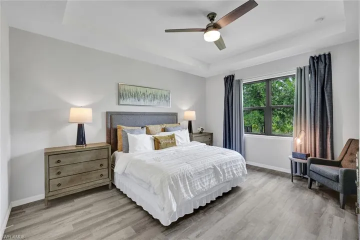 Spacious room featuring wood-finish flooring, a tray ceiling, and a ceiling fan with integrated lighting