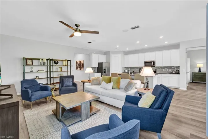 Open-concept living space featuring wood-finish flooring, a contemporary ceiling fan with integrated lighting, recessed lighting, and a kitchen with white cabinetry and a tile backsplash