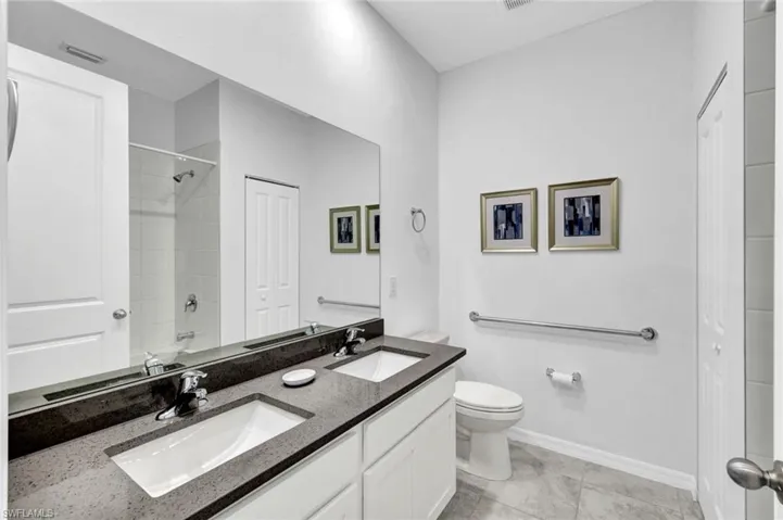Bathroom featuring a dual vanity with a dark stone-finish countertop, undermount sinks, and chrome faucets